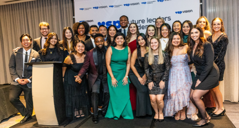 The 2025 VSP Future Leaders Academy graduating cohort poses on stage in front of the VSP Future Leaders Academy Banner looking at the camera and smiling.