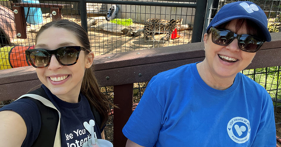VSP Vision employees Kiley B. and Rochelle B. volunteered at the Folsom City Zoo Sanctuary for Global Volunteer Month. Both are wearing blue VSP-branded shirts and laughing.